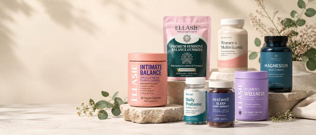 A group of ELIASIe wellness supplements arranged on a light stone surface with soft botanical props. The products include pink, green, white, blue, and purple bottles and jars, with visible labels such as Intimate Balance, Women's Multigrain, Magnesium, and Restwell Sleep.