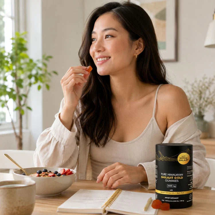 Woman seated at a table beside a black bottle of Shilajit gummies, an open notebook and a bowl of fruit.