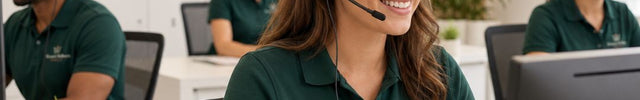 A woman in a green polo shirt with a headset works at a computer in a bright office, with other employees and the Women's Wellness Direct logo visible in the background.